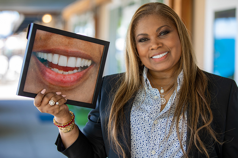 Magnolia, an african-american woman, smiling after full mouth reconstruction holding a before portrait.