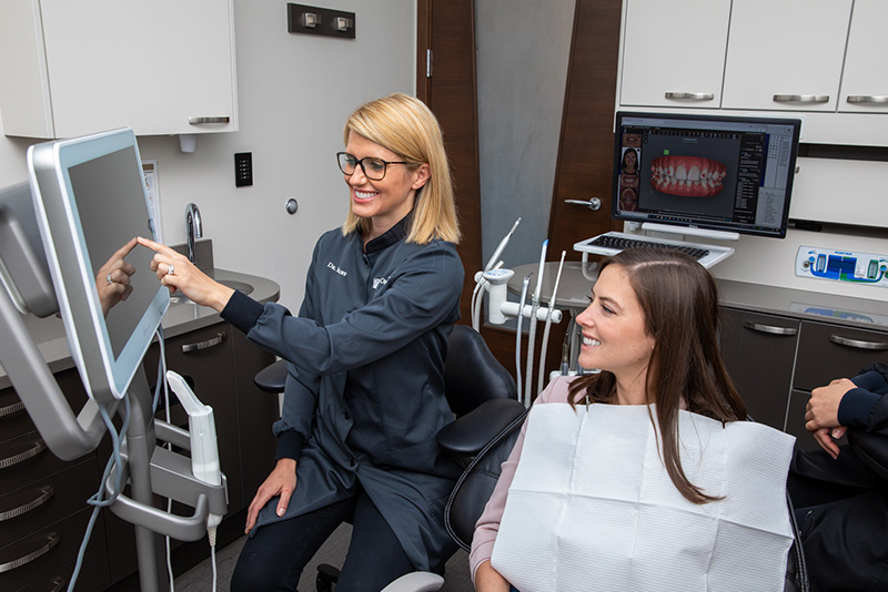 Orthodontist, Dr. Brienne Roloff pointing at monitor while female patient sits in dental chair.