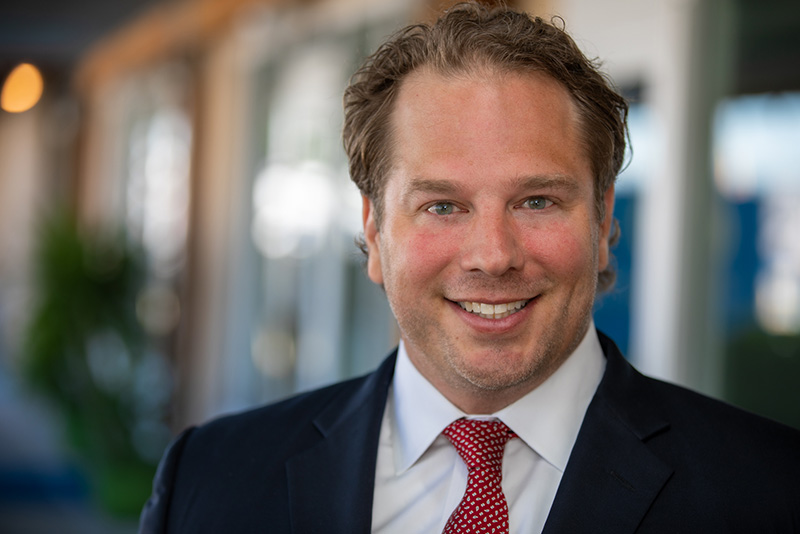 Smiling prosthodontist Dr. Dean Kois wearing navy suit and red tie.