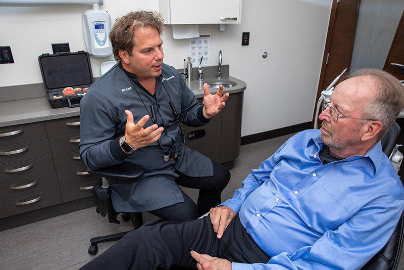 Prosthodontist Dr. Dean Kois discussing full arch dental implant treatment plan with elderly male patient in a dental chair.