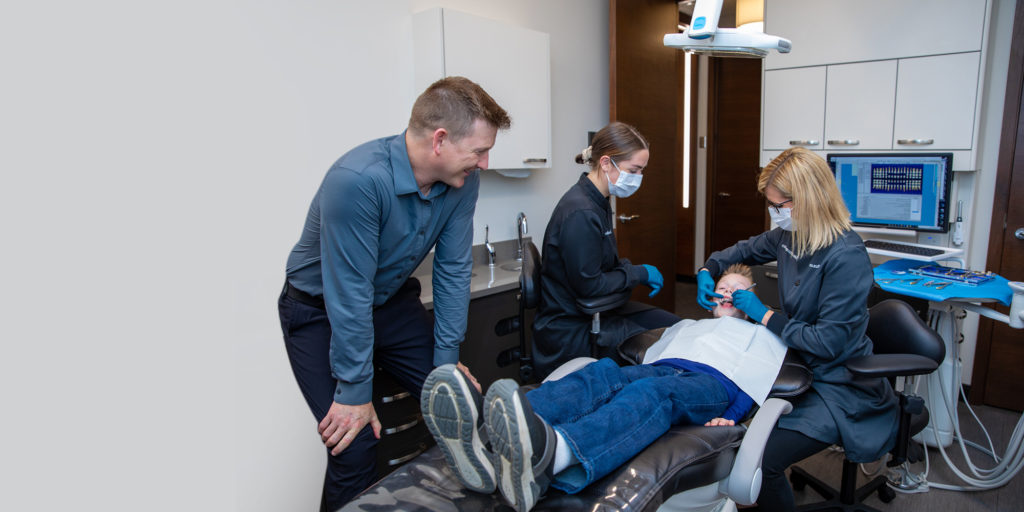 Father watching his freckled son under go orthodontic braces treatment by Dr. Brienne Roloff.