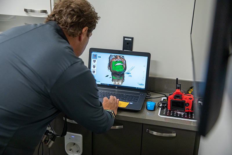 Prosthodontist Dr. Dean Koise looking at laptop with 3D smile design software showing a patient's face.