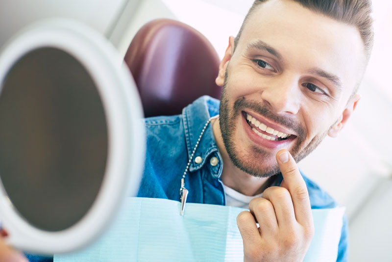 dental patient smiling looking in hand-held mirror.